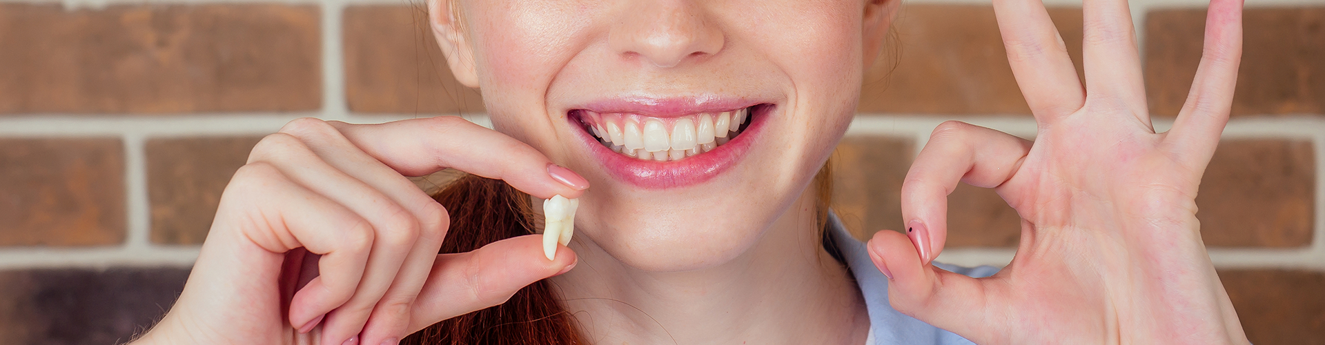 smiling woman holding extracted tooth and making ok sign.